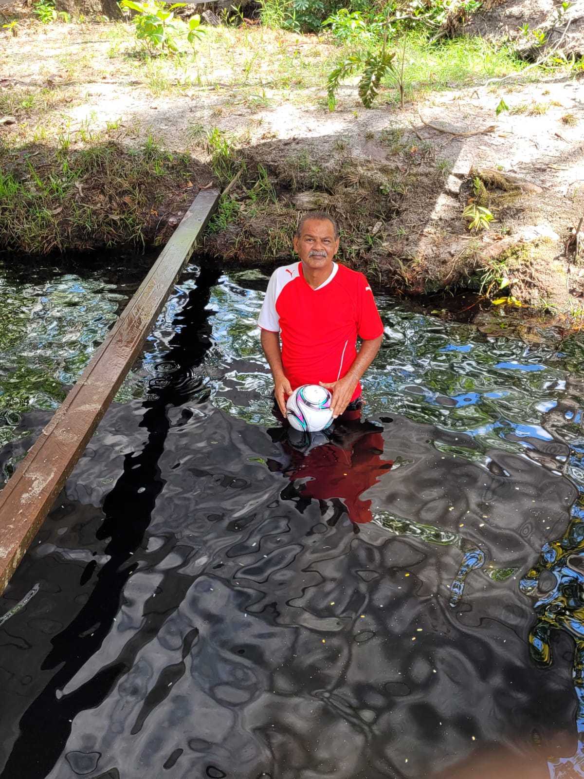 Mohamed Haroenkhan Abdul standing in a creek with a football